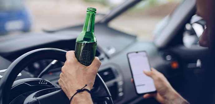 Drunk driver drinking alcohol in car and using smartphone