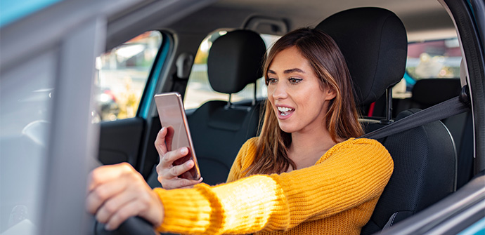 Texting and driving behind the wheel Breaking the law Woman driving car distracted by her mobile phone