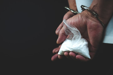 person's hands in handcuffs holding bag of drugs