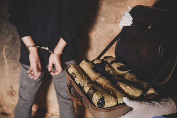 man in handcuffs and pile of drugs